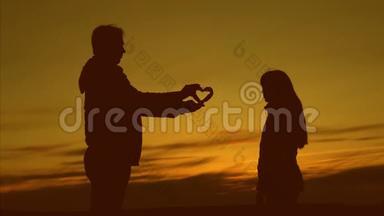 一个父亲在日落时把他的心献给一个孩子的剪影。 父亲`爱他的女儿。 孩子的父母。 这就是